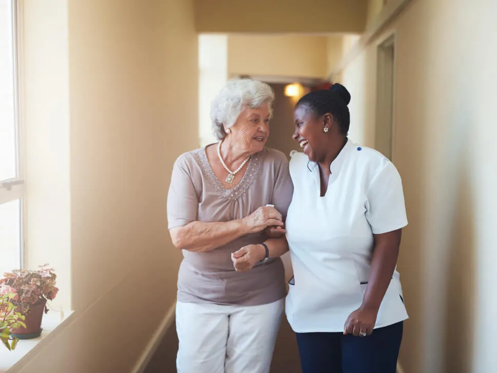 Une préposée riant aux éclats accompagne une personne âgée dans un corridor de la résidence