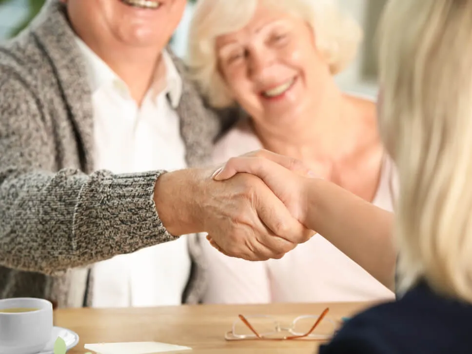 Un couple d’ainés serrent la main à une conseillère en aide et subventions